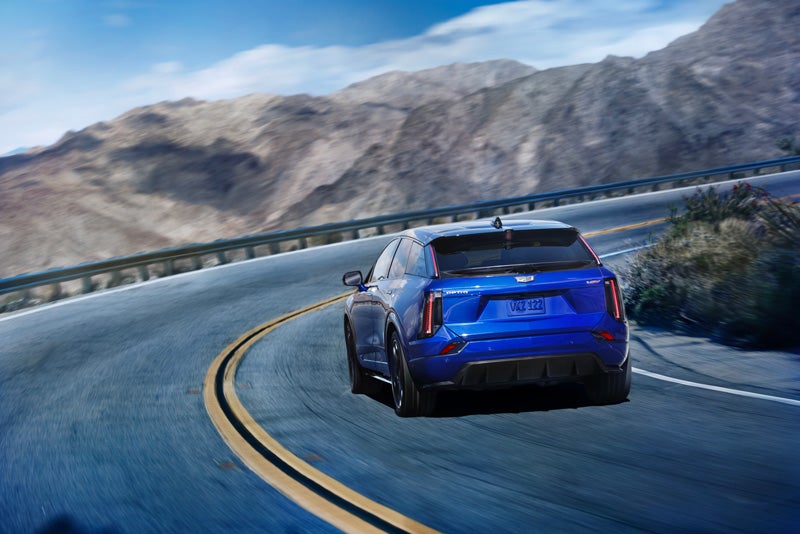 Rear View of a Blue 2026 OPTIQ-V Driving on a Curve of a Mountain Row | Peterson Cadillac in BOISE ID